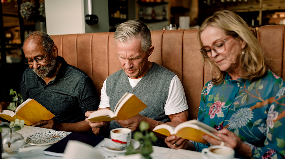 Senior men and woman reading books while sitting in cafe